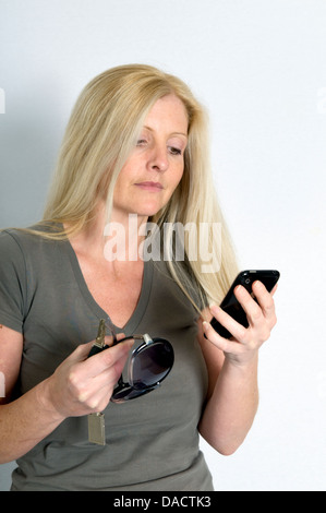 Kaukasische Frau mit Handy, Autoschlüssel und Sonnenbrille vor einem weißen Hintergrund Stockfoto