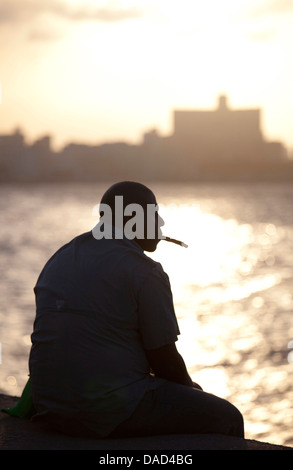 Mann halb Silhouette saß auf dem Deich bei Sonnenuntergang, eine Zigarre rauchend, den Malecon, Havanna Centro, Havanna, Kuba, Westindische Inseln Stockfoto