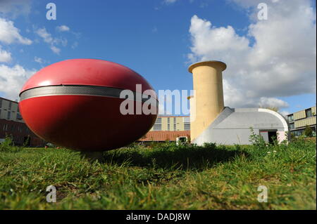 Ein rotes elliptisches Objekt, das die Soundinstallation Luft getragen gehört befindet sich vor einer Motor-Prüfstand an der Aerodynamik-Park auf dem Campus der Humboldt-Universität Berlin in Berlin-Adlershof, Deutschland, 13. Oktober 2011. Der Motor-Prüfstand für wissenschaftliche Zwecke in den 1930er Jahren errichtet und ist heute ein Denkmal, die Besucher über die Geschichte der erinnern soll die Stockfoto