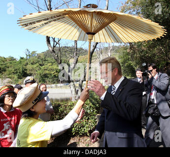 Eine japanische Frau, die einen traditionellen militärischen Hut übergibt einen Sonnenschirm an Bundespräsident Christian Wulff im ehemaligen Kriegsgefangenenlager des ersten Weltkrieges namens Bando, wo deutsche Soldaten im Gefängnis, unter anderem in Naruto, Japan, 27. Oktober 2011 ausgetragen wurden. Wulff legte einen Kranz an der Gedenkstätte. Das Staatsoberhaupt ist bei einem sechstägigen Besuch in Japan. Foto: Wolfgang Ku Stockfoto