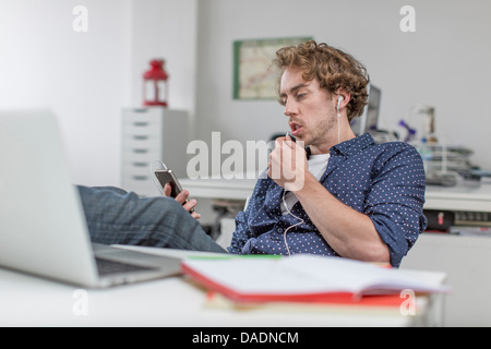 Junge Büroangestellte anhören von MP3-Player am Schreibtisch Stockfoto