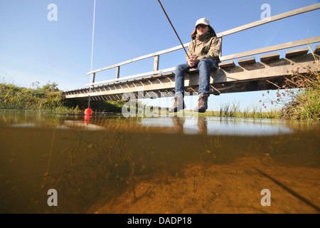 Junge sitzt auf einer hölzernen Brücke und Angeln, Niederlande, Norden der Niederlande Stockfoto