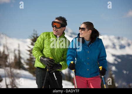 Junge Frau und reifer Mann in Skibekleidung holding Skistöcke Stockfoto