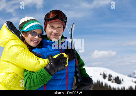 Junge Frau in Skibekleidung umarmen reifer Mann hält Ski, Porträt Stockfoto