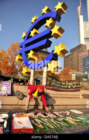 Ein Demonstrant schreibt auf dem Boden vor dem Euro-Symbol auf dem Gelände der Protest-Camp in Frankfurt Am Main, Deutschland, 8. November 2011. Die Demonstranten wollen die Macht des Kapitalismus zu verkleinern und geben Auskunft über die getroffene Probleme des Finanzmarktes. Sie modellieren selbst nach den USA amerikanische "Occupy Wall Street"-Bewegung. Foto: MARC TIRL Stockfoto