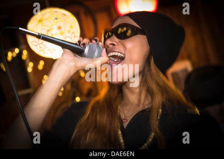 Frau mit Hut und Sonnenbrille im Mikrofon singen Stockfoto