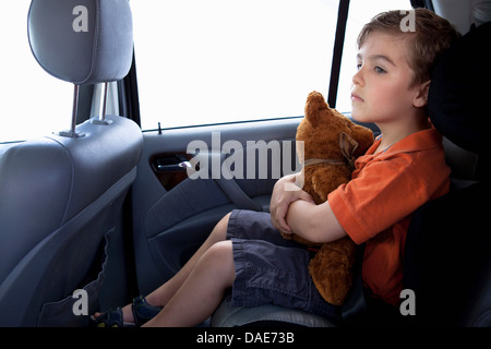 Junge im Kindersitz im Auto halten Teddybär Stockfoto