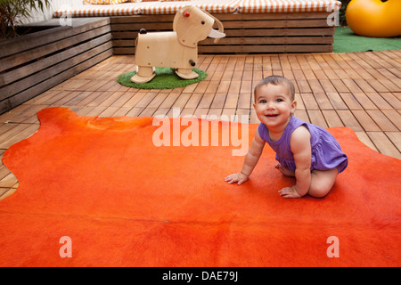 Babymädchen kriecht auf orange Teppich, Porträt Stockfoto