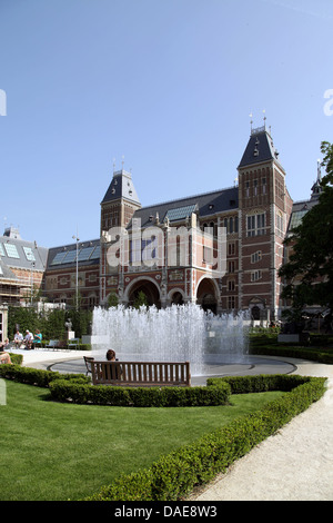 Sonniger Blick auf die Gärten des Rijksmuseums mit Wasserbrunnen, üppig grünen Hecken, Menschen, die sich auf Bänken vor der Kulisse des Museums entspannen. Stockfoto