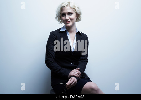 Studio-Porträt der blonden Geschäftsfrau auf Hocker sitzend Stockfoto