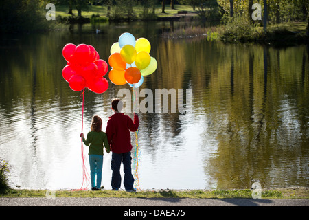 Bruder und Schwester vor See mit Trauben von Luftballons Stockfoto