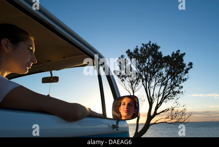 Junge Frau, die aus Camper van Fenster in der Abenddämmerung Stockfoto