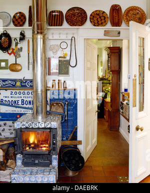 Holzofen mit blau + weiß gefliesten Surround im Landhaus-Küche mit rustikalen Keramik-Platten im Regal über der Tür Stockfoto