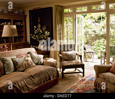Gemusterte Kissen und werfen auf Sofa im Ferienhaus Wohnzimmer mit Sessel neben französischen Fenster zum Garten Stockfoto