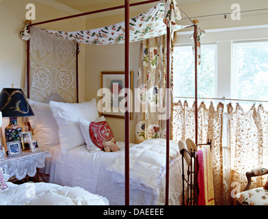 Floral Baldachin auf Metall Schlafzimmereinrichtungen Bett mit weißen Kissen und Bettwäsche im Landhaus Schlafzimmer mit floral Café Vorhänge am Fenster Stockfoto