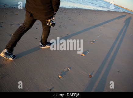 Beine eines Mannes in schwarz zu Fuß am Strand mit seiner Kamera gekleidet Stockfoto