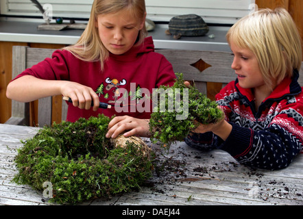 jungen und Mädchen binden Moos mit Draht an einen Kranz aus Stroh für die Adventszeit, Deutschland Stockfoto