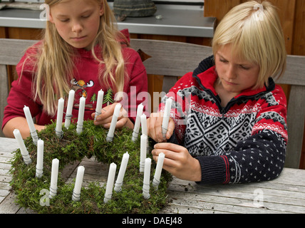 Kinder kleben Kerzen auf einem Kranz für die Adventszeit, Deutschland Stockfoto