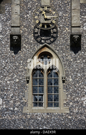 Eine große Uhr auf ein Kirchengebäude mit Bleiglas Fenster unten und zwei Stein geschnitzte Gesichter gebietsübergreifenden die Uhr. Stockfoto