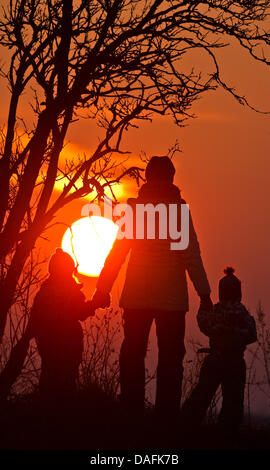 Eine Frau geht mit ihren beiden Kindern entlang einer Landstraße vor der Kulisse eines Romatnic Evenbing Himmels in der Nähe von Petersdorf, Deutschland, 21. Februar 2011. Foto: Patrick Pleul Stockfoto