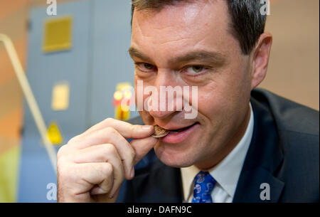 Der bayerische Finanzminister, Markus Soeder, beißt sich auf die neue Euro-Münze "2 Euro - 10 Jahre Euro" an der kaiserlichen Münze in München, 6. Dezember 2011. Bei der Bayerischen kaiserliche Münze wurden die ersten deutschen Euro-Münzen im Jahr 2002 geprägt. Foto: SVEN HOPPE Stockfoto