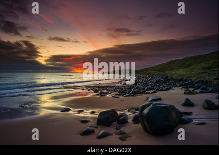 Vor Sonnenaufgang an der Northumberland Küste mit Dunstandburgh Castle in der Ferne Licht. Stockfoto