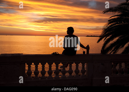 Ein Mann sitzt auf einem Geländer durch den Rio Plata trinken Yerba Matetee in Colonia del Sacramento, Uruguay Stockfoto