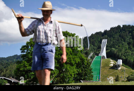 (Dpa-Datei) Ein Datei-Bild datiert 9. August 2010 eines Bauern zu Fuß mit einer Sense vor der Olympiaschanze in Garmisch-Partenkirchen. Deutschland. Foto: Marc Müller Stockfoto