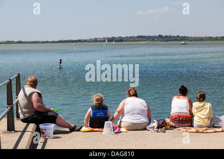 Familie Gruppe von großen Leute sitzen am Deich auf dem Kai am Mudeford Verdrehungen. Stockfoto