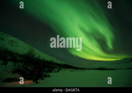 Aurora-Welle vor der bestirnte Himmel über tief verschneiten Tal mit ein Naturfotograf Ausrüstung im Schnee, Kattfjordeidet, Kvaloea, Troms, Norwegen Stockfoto