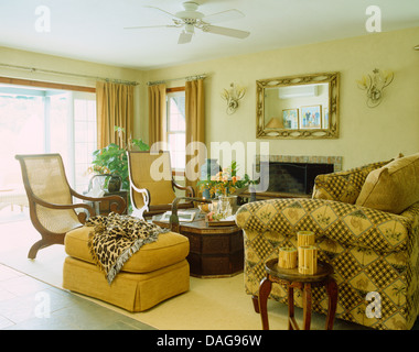 Animal-print zu werfen, auf gelbe Ottomane im Wohnzimmer mit Planter es Stühle und gemusterten Sofa unter Deckenventilator Stockfoto