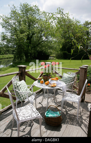 Schmiedeeisen Tisch und Stühlen mit grünen aufgegebenes Kissen auf überdachten Balkon mit Blick auf Rasen im Garten Stockfoto