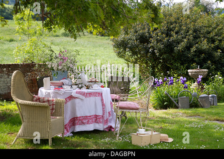 Lloyd Loom Stuhl neben Tisch mit weißen Tuch eingefasst mit rot auf Rasen im Garten im Sommer Stockfoto