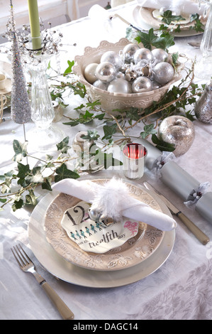 Schüssel mit silbernen Kugeln in Schale auf den Tisch für Weihnachtsessen mit weißen Teller und nachgestellte Efeu auf dem weißen Tuch Stockfoto