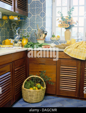 Korb mit Obst am Boden neben dunklem Holz ausgestattet Einheiten in Küche mit gemusterten blau gekachelte Wand Stockfoto