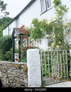 Stein-Wand und Metall-Gate vor Berghütte mit Rosen rund um Tür und Fenster Stockfoto