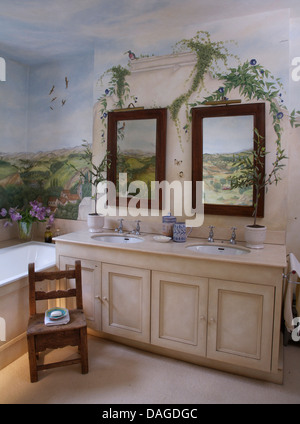 Paar Außenspiegel oberhalb Waschtischunterbau mit doppelten Waschbecken im Badezimmer mit kleinen hölzernen Stuhl und gemalten Landschaft Wandbild Stockfoto