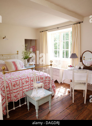 Kleine blaue Tabelle unten Antik Messing-Bett mit rosa + weiße Decke im Land Schlafzimmer mit Holzboden und kleinen Schminktisch Stockfoto