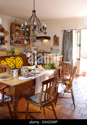 Metall Kronleuchter über Kiefer Tisch und einfachen Holzstühlen im französische Landküche mit gefliesten Terrakotta-Böden Stockfoto