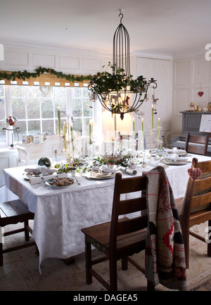 Metall Kronleuchter über Holzstühle und Tisch mit weißen Leinentuch set für Weihnachtsessen im Land Speisesaal Stockfoto