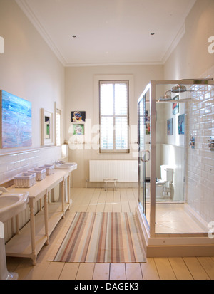 Paar Sockel Becken und einfachen Holztisch im modernen Badezimmer mit großer Duschkabine und gestreiften Teppich Stockfoto