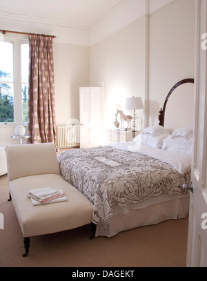 Weiß gepolsterte Chaiselongue am Fuße des Doppelbett mit weißen Kissen und grau gemusterten Bettdecke in weiße Schlafzimmer Stockfoto