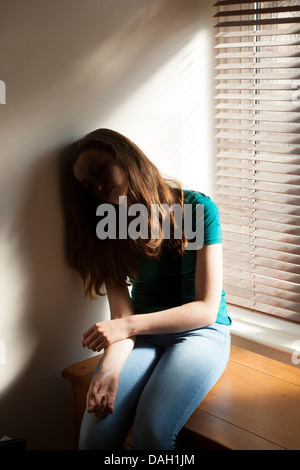 Ein junges Mädchen, sackte sitzen gegen die Wand durch ein Fenster mit Licht herein. Stockfoto
