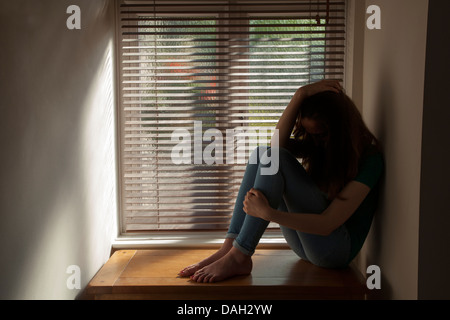 Ein junges Mädchen die hand auf dem Kopf, sitzen an einem Fenster mit Licht herein. Modell und der Eigenschaft freigegeben. Stockfoto