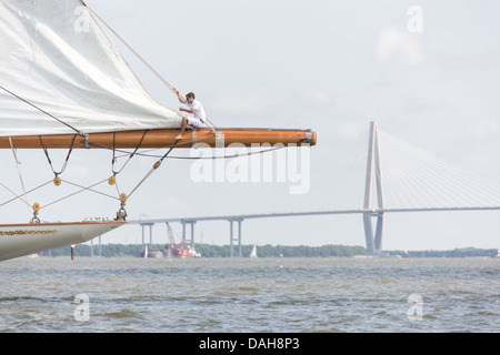 Eine Deck Hand rigs die Segel auf die 196-Fuß Segelyacht Germania Nova als es Charleston Harbor mit der Arthur Ravenel Jr. Bridge im Hintergrund 26. Juni 2013 in Charleston, South Carolina Segel. Stockfoto