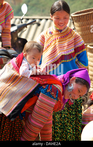 Flower Hmong Frau mit Kind im Tragetuch auf ihrem Rücken, können Cau Markt, in der Nähe von Bac Ha, Provinz Lao Cai, Vietnam Stockfoto