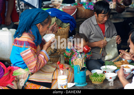 Flower Hmong Familie essen, an einem Stand im Bereich der Markt von Bac Ha, Provinz Lao Cai, Vietnam. Kind mit Stäbchen Stockfoto