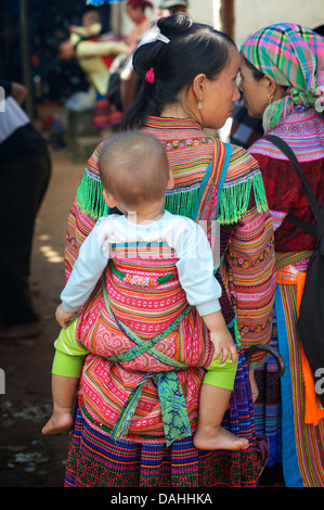 Flower Hmong Frau Baby in handgewebte Babytrage tragen. COC Ly Markt, Nord-Vietnam Stockfoto
