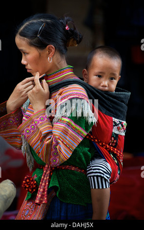 Flower Hmong Frau in markanten tribal Kostüm, mit einem Kind auf dem Rücken. COC Ly, Vietnam Stockfoto