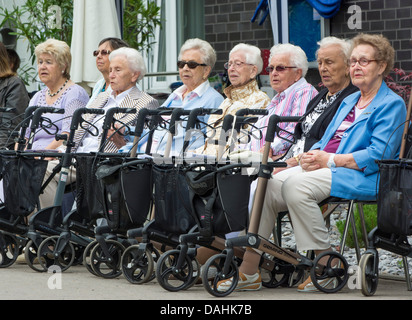 Acht alte Frauen sitzen vor einer Seniorenresidenz mit ihren Rollatoren / Wanderer auf Rädern / Gehhilfe vor ihnen. Stockfoto